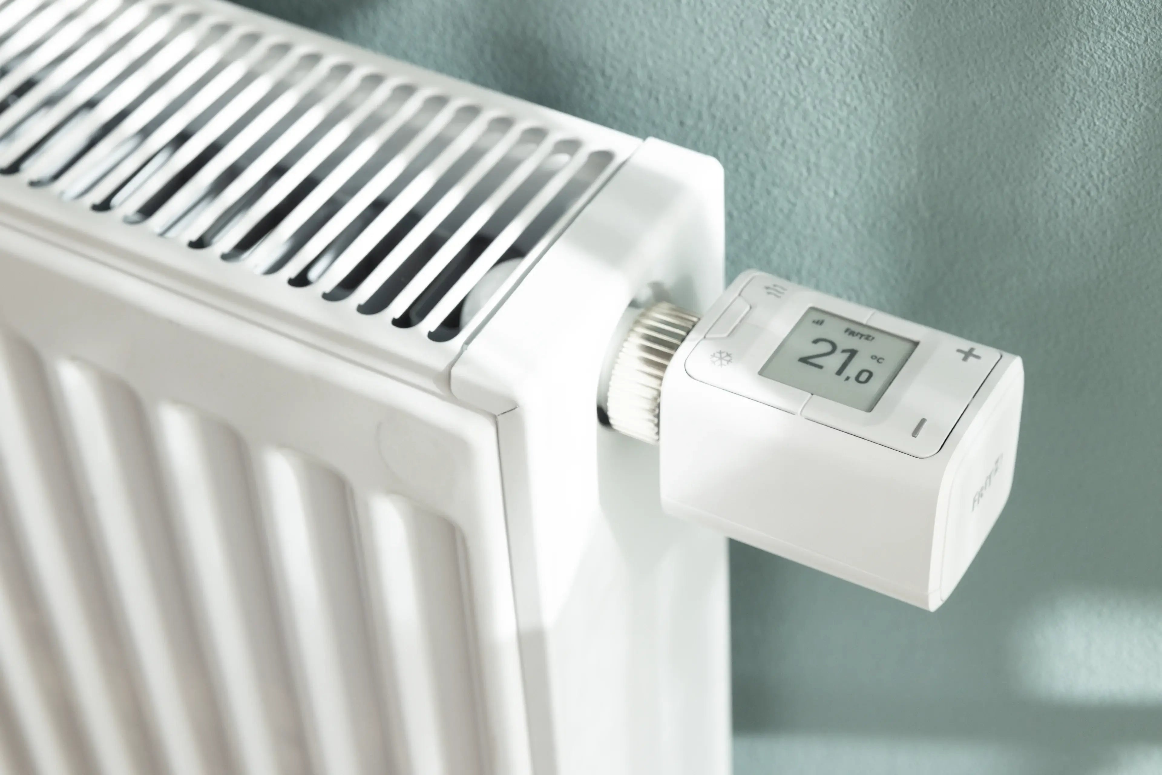 Moderne Heizkörpersteuerung mit digitalem Thermostat zeigt 21 Grad Celsius auf weißem Heizkörper.