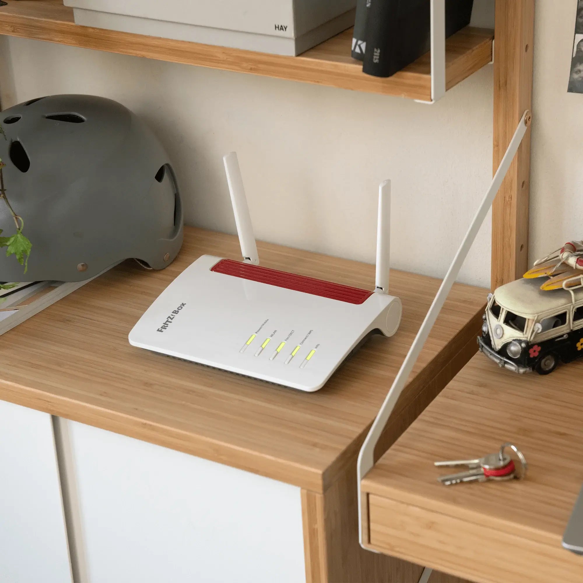 FRITZ!Box 6850 5G-Router auf einem Holztisch mit grauem Helm im Hintergrund, zeigt die LED-Anzeige.